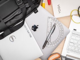 An overhead view of an assortment of laptops including Dell, Apple MacBook, and Lenovo Yoga with stationery items, illustrating a typical teacher's workspace.