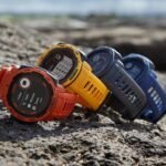 An array of Garmin watches in orange, yellow, blue, and gray, perfectly positioned on rocky terrain, highlighting the best Garmin watch selections for every lifestyle.