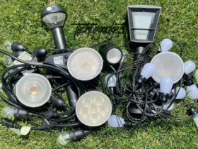 A diverse array of the best outdoor smart light bulbs and fixtures scattered on the grass, showcasing different shapes and sizes for customized lighting setups.
