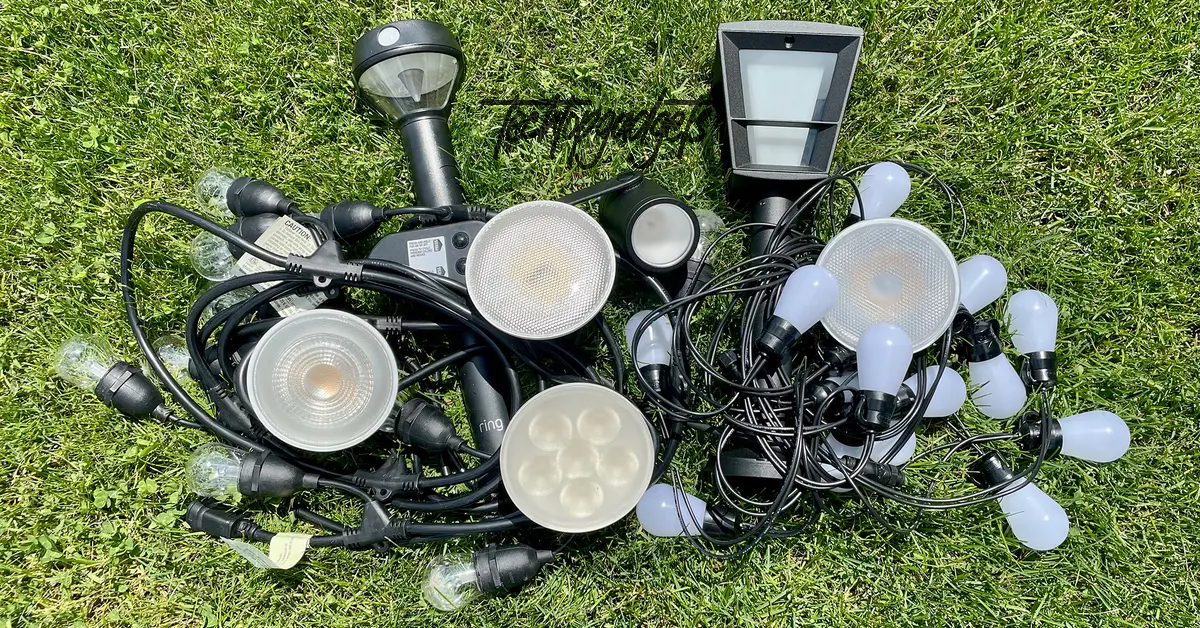 A diverse array of the best outdoor smart light bulbs and fixtures scattered on the grass, showcasing different shapes and sizes for customized lighting setups.