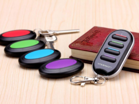 A Vodeson remote key finder placed next to its colorful receivers attached to keys and a book, representing the best key finder for elderly users for easy retrieval of their items.