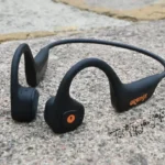 A pair of best bone conduction headphones with a microphone, featuring a bold orange logo, laid out on urban concrete, perfect for city adventurers who want to stay connected while on the go.