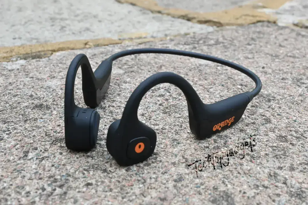 A pair of best bone conduction headphones with a microphone, featuring a bold orange logo, laid out on urban concrete, perfect for city adventurers who want to stay connected while on the go.
