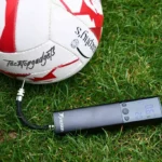 The best electric ball pump in action, showcasing its digital display with clear PSI reading while attached to a soccer ball, ensuring precise inflation on the grassy field.