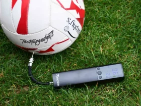 The best electric ball pump in action, showcasing its digital display with clear PSI reading while attached to a soccer ball, ensuring precise inflation on the grassy field.
