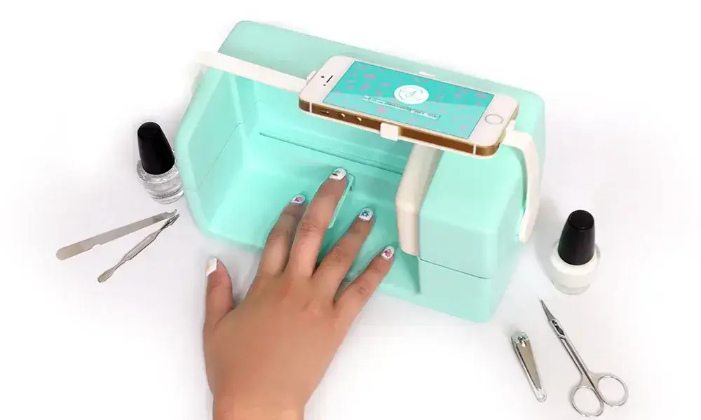 A compact mint-green nail dryer with multiple features including a smartphone holder, showcasing its nail dryer features alongside manicure tools and polishes.