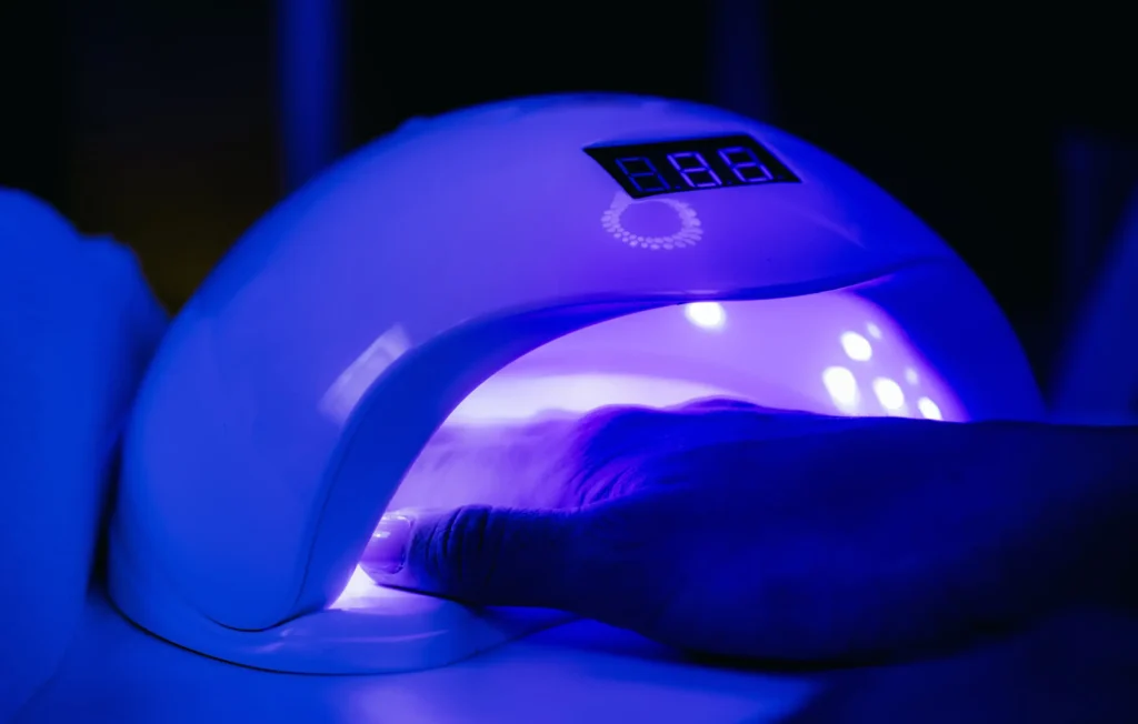 Close-up of a hand placed inside a UV nail dryer emitting a purple light, signifying the importance of proper curing in nail art design for a flawless finish.