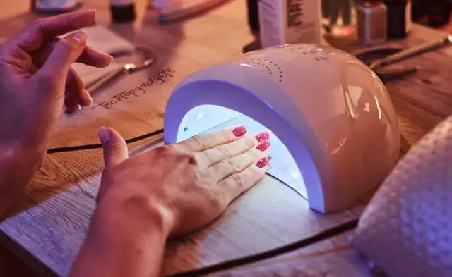 Ambient setting with a hand being placed under a UV nail dryer, emphasizing the convenience and effectiveness of home nail artistry with the aid of UV technology.