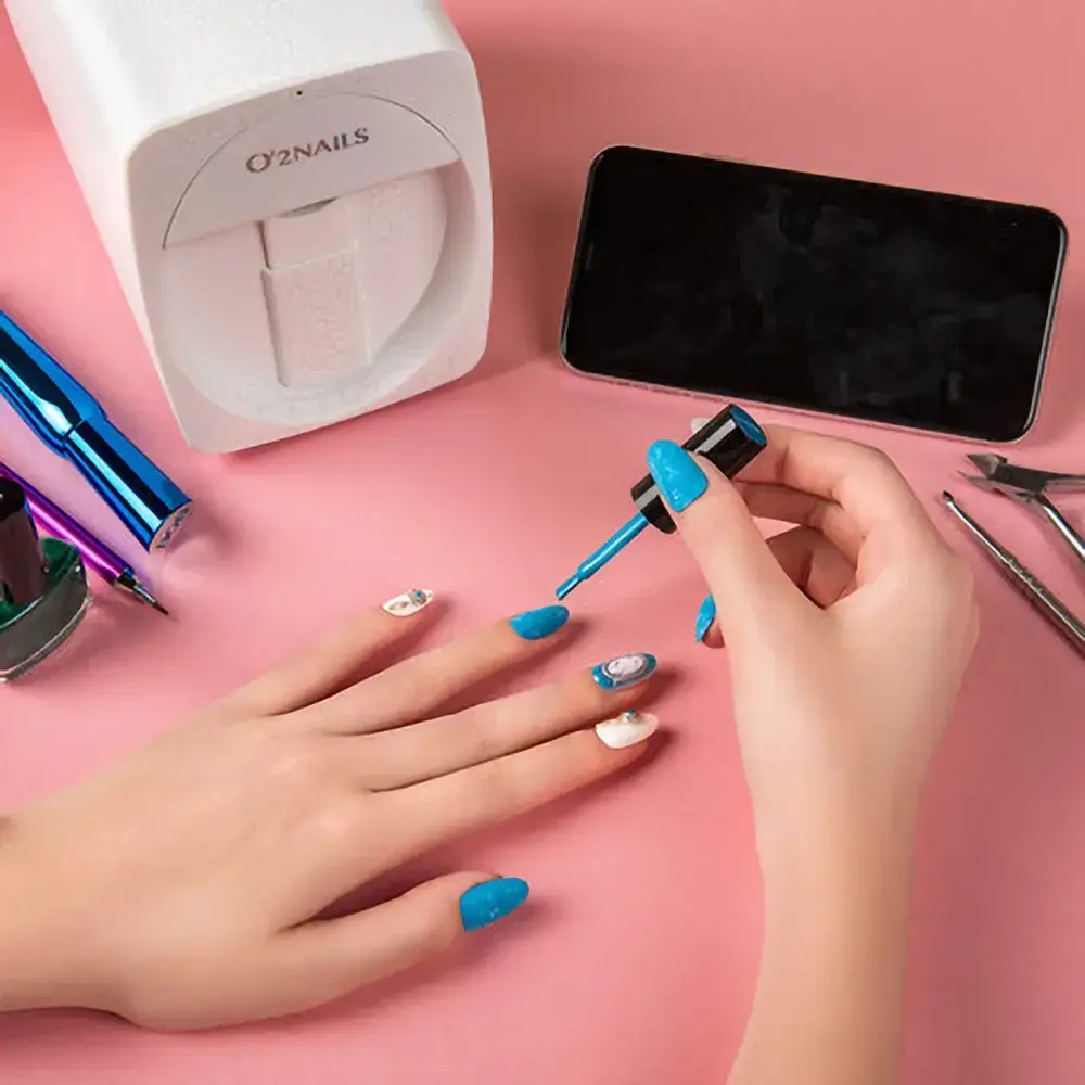 A well-manicured hand is depicted in the process of applying nail polish, with a digital nail art printer in the background. The image captures the user's engagement with the device and emphasizes the importance of regular cleaning for optimal functionality.