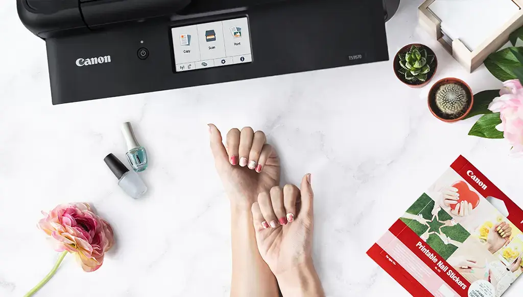 A neatly manicured hand rests beside a digital nail art printer and nail polish, highlighting the convenience of at-home beauty technology while prompting discussions on the long-term health effects, including cancer, of using such devices.