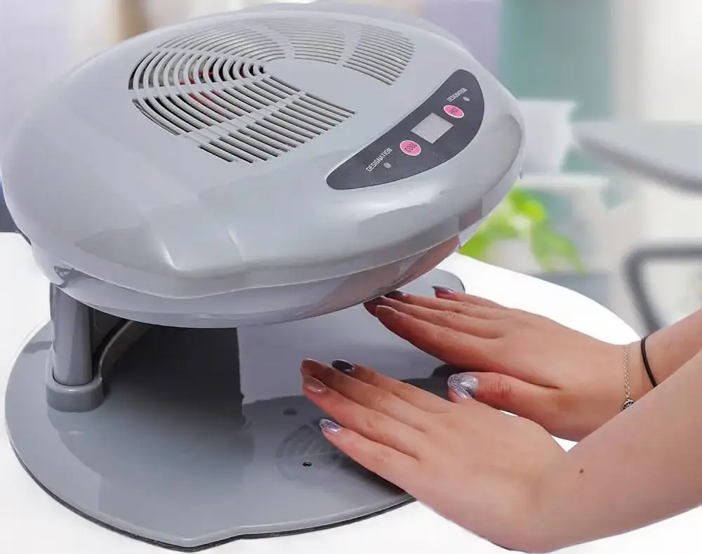 Hands under a streamlined gray air nail dryer, demonstrating ease of use for drying modern nail art creations.