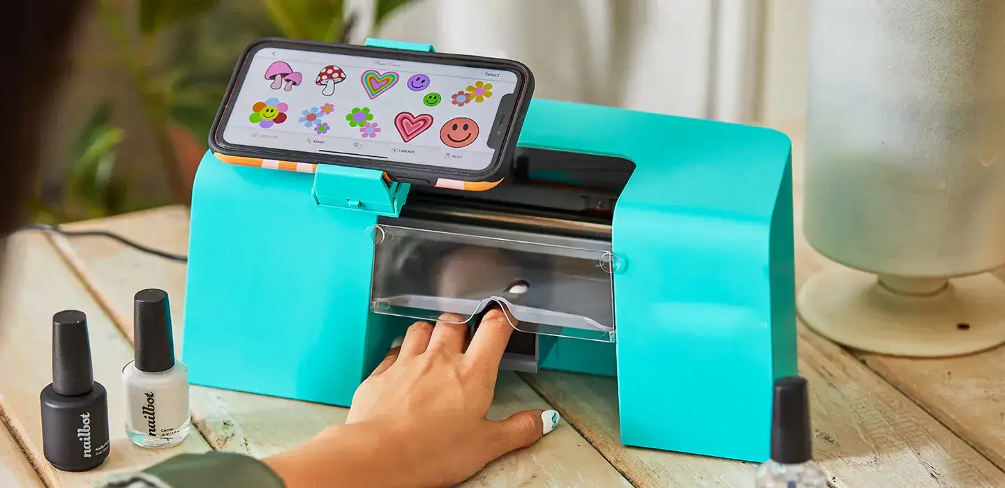 A person selects a nail design on their smartphone, which is attached to a bright turquoise nail art printer, demonstrating the ease of choosing digital nail art for personalized fashion statements.