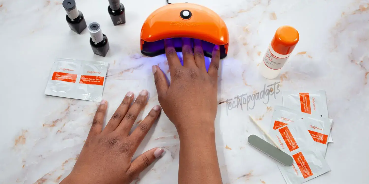 A hand placed under an orange nail dryer, with nail care products surrounding it, illustrating practical nail dryer tips and tricks for achieving top nail art trends.